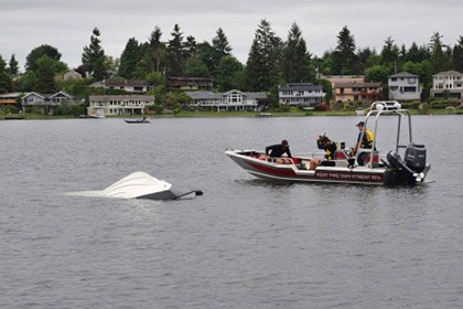 Firefighters tow a capsized boat to shore at Lake Meridian early Monday. The two men in the boat were able to swim safely to a dock.