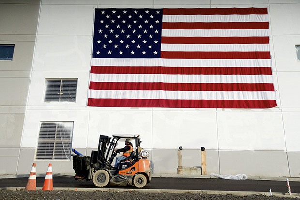 A construction worker drives a work truck underneath the giant American flag hung outside of the new Amazon warehouse in the Kent industrial district.