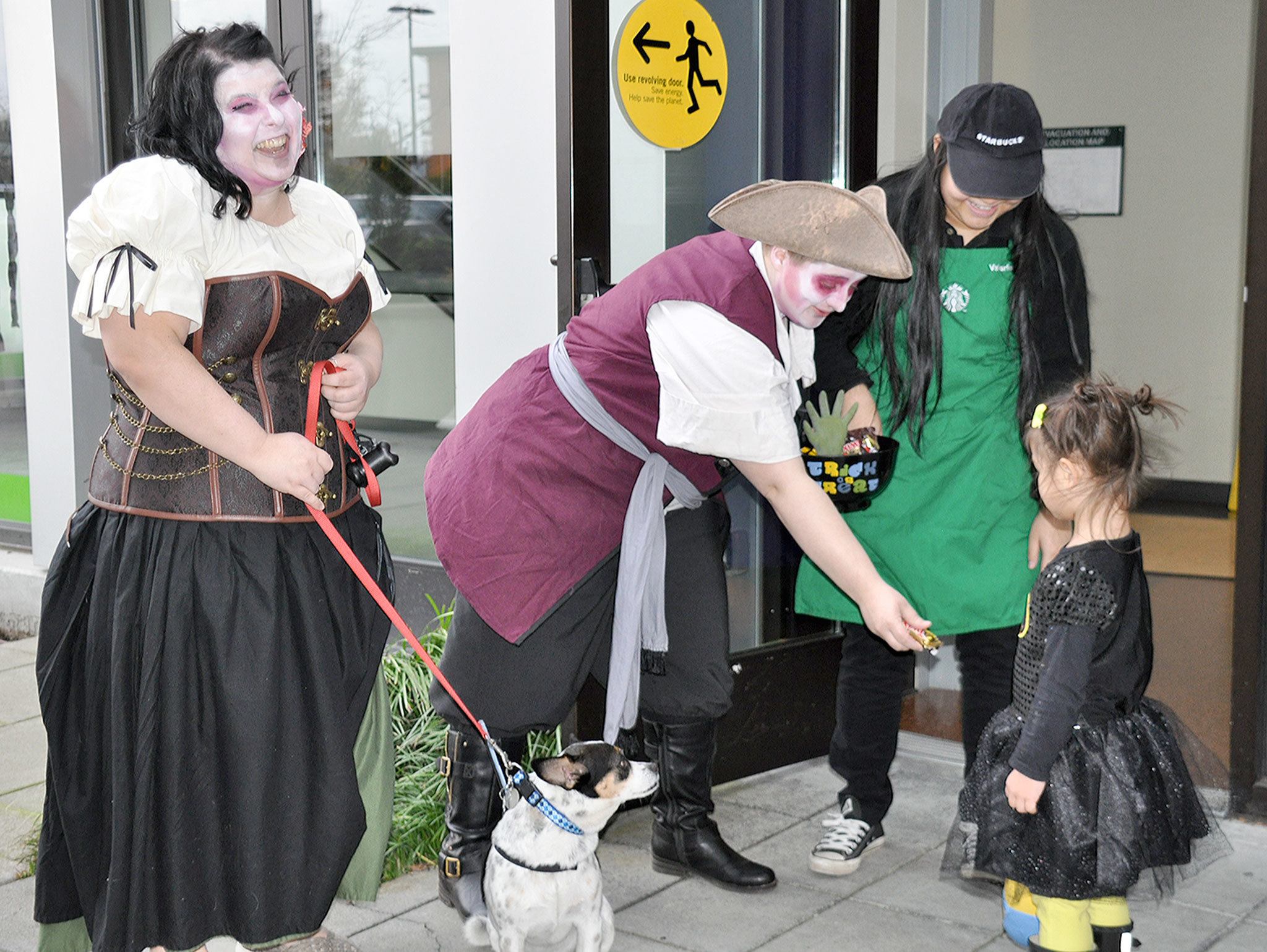 From left, Mary Dempsey, Fluke the dog, Katie Mathews and Valerie Phanissay hand out candy to trick-or-treaters at Green River College’s campus at Kent Station on Monday evening. HEIDI SANDERS, KENT REPORTER