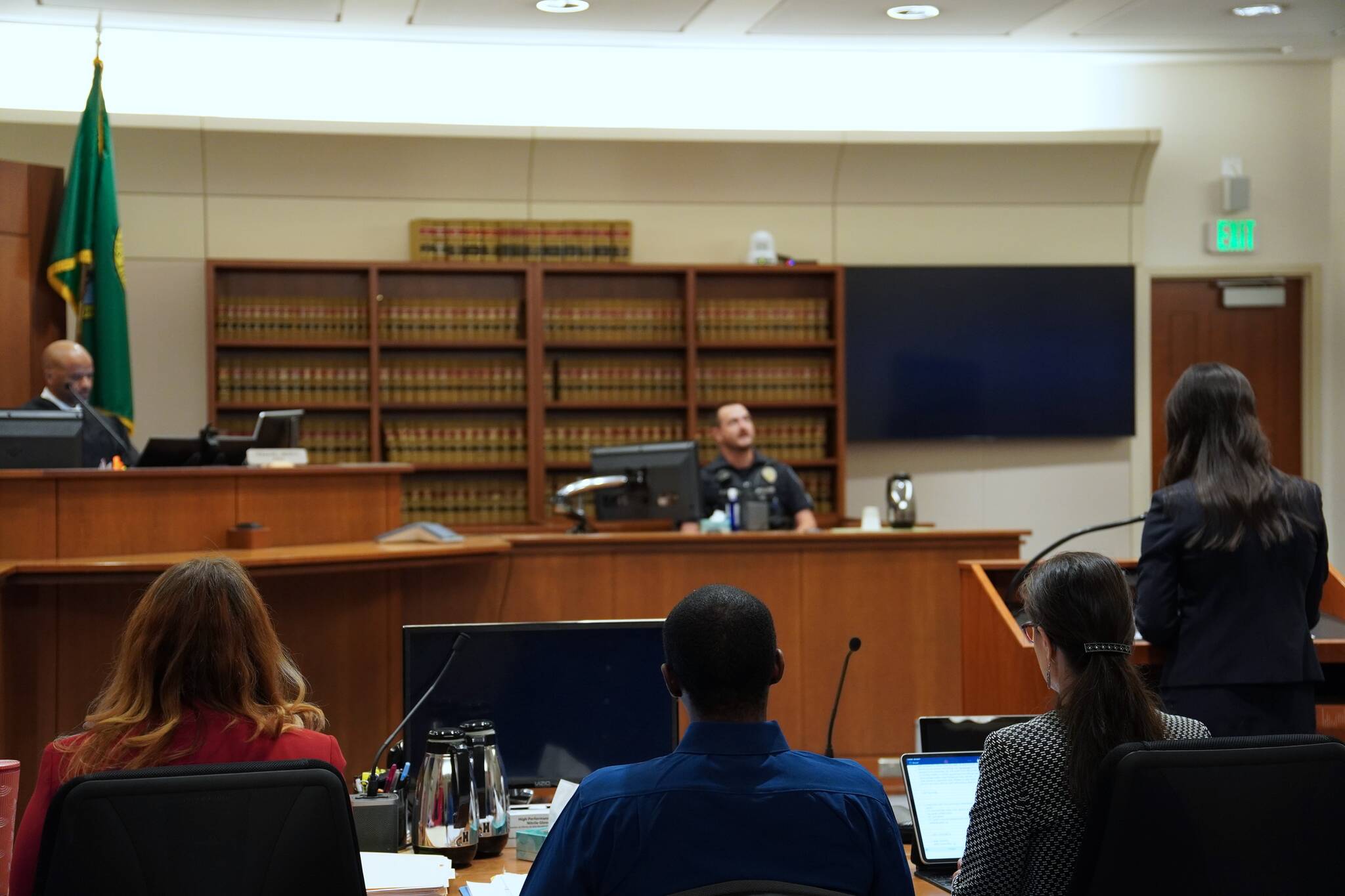 Photo by Joshua Solorzano/The Mirror
Corniche Washington is in the middle, wearing a blue shirt between his counsel, while prosecutor Jacqueline Lawrence speaks to an officer who responded to the scene.